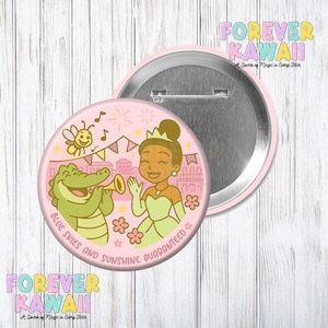 May include: A pink button with a cartoon illustration of a princess, an alligator playing a trumpet, and a bee. The text "BLUE SKIES AND SUNSHINE GUARANTEED" is printed around the edge. The button has a silver back and a pink border. The words "FOREVER KAWAII" are also printed on the button.