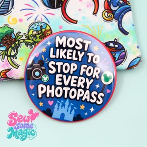 May include: A circular button with a dark blue background featuring the white text "MOST LIKELY TO STOP FOR EVERY PHOTOPASS". The design includes a black camera icon, a light blue castle silhouette, small pink hearts, yellow stars, and green icons.