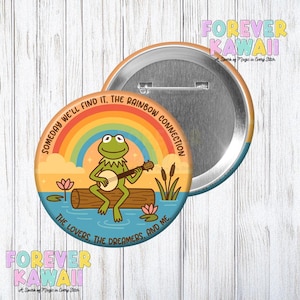 May include: A round button featuring a cartoon frog playing a banjo on a log in water, with a rainbow and text that reads "Someday We'll Find It, The Rainbow Connection" and "The Lovers, The Dreamers, And Me." The button has a metal back and a pin.