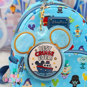 May include: A light blue Disney Parks mini backpack with a matching Mickey Mouse ear-shaped keychain. The keychain has the text "BEST CRUISE EVER!" and a cartoon ship graphic. The backpack features Disney character patterns.