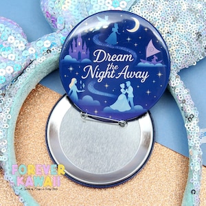 May include: A round, blue button with the text "Dream the Night Away" and illustrations of a castle, characters, and a boat. The button is open, revealing a silver, metallic back. The button is next to a sequined headband.