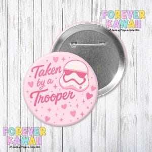 May include: A pink badge with the phrase "Taken by a Trooper" and a cartoon Stormtrooper helmet wearing sunglasses. The badge is decorated with hearts and stars. The words "Forever Kawaii" are also visible.