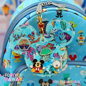 May include: A light blue backpack with a Mickey Mouse ear-shaped charm featuring various Disney character pins. The charm is attached with a gold-colored clasp. The text "FOREVER KAWAII" is visible on the backpack.