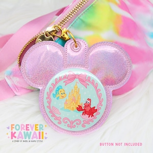 May include: A lavender glittery Mickey Mouse-shaped keychain with a round button featuring Ariel, Flounder, and Sebastian from The Little Mermaid. The keychain is attached to a pink bag with a gold zipper. The text "FOREVER KAWAII" is visible.