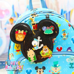 May include: Black Mickey Mouse-shaped keychain with various character pins. The pins include Winnie the Pooh, Donald Duck, Chip and Dale, and a turtle. The keychain is attached to a light blue backpack with a Disney theme. The text "FOREVER KAWAII" is visible.