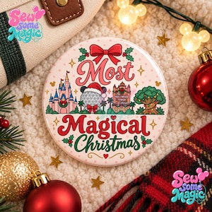 以下が含まれることがあります： 薄いピンクの背景に赤いリボンと「Most Magical Christmas」の文字が描かれた丸い缶バッジ。城、サンタ帽をかぶったジオデシックドーム、ホテル、ライトアップされた木のイラストがデザインされています。