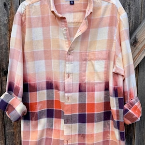 May include: A button-down plaid shirt in shades of peach, orange, and purple. The shirt has a pocket on the chest and the sleeves are rolled up. The brand name "Club Room" is visible on the label.