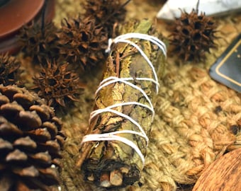 May include: A bundle of dried herbs wrapped in white twine, with a brown, woven surface in the background.