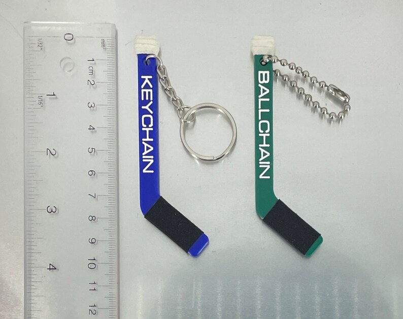 May include: Two hockey stick keychains, one blue with the word "KEYCHAIN" and one green with the word "BALLCHAIN".