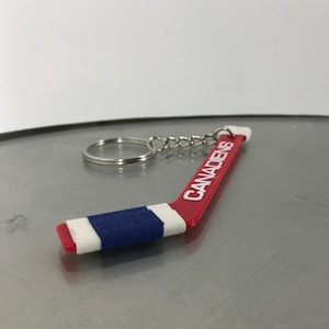 May include: A red and blue hockey stick keychain with the word "Canadiens" printed on it in white.