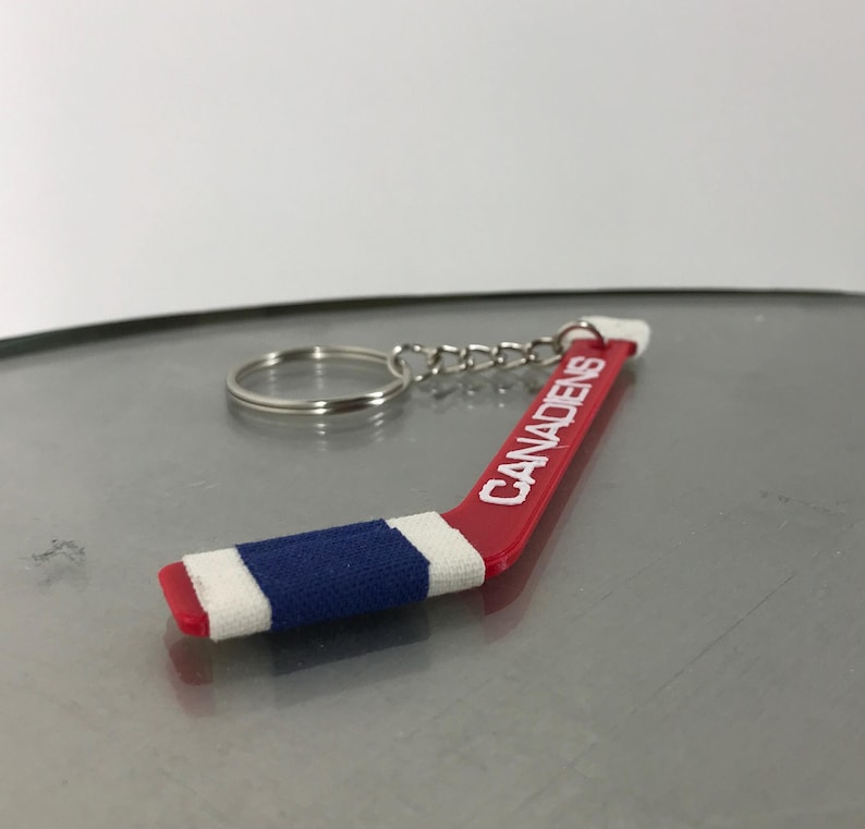 May include: A red and blue hockey stick keychain with the word "Canadiens" printed on it in white.