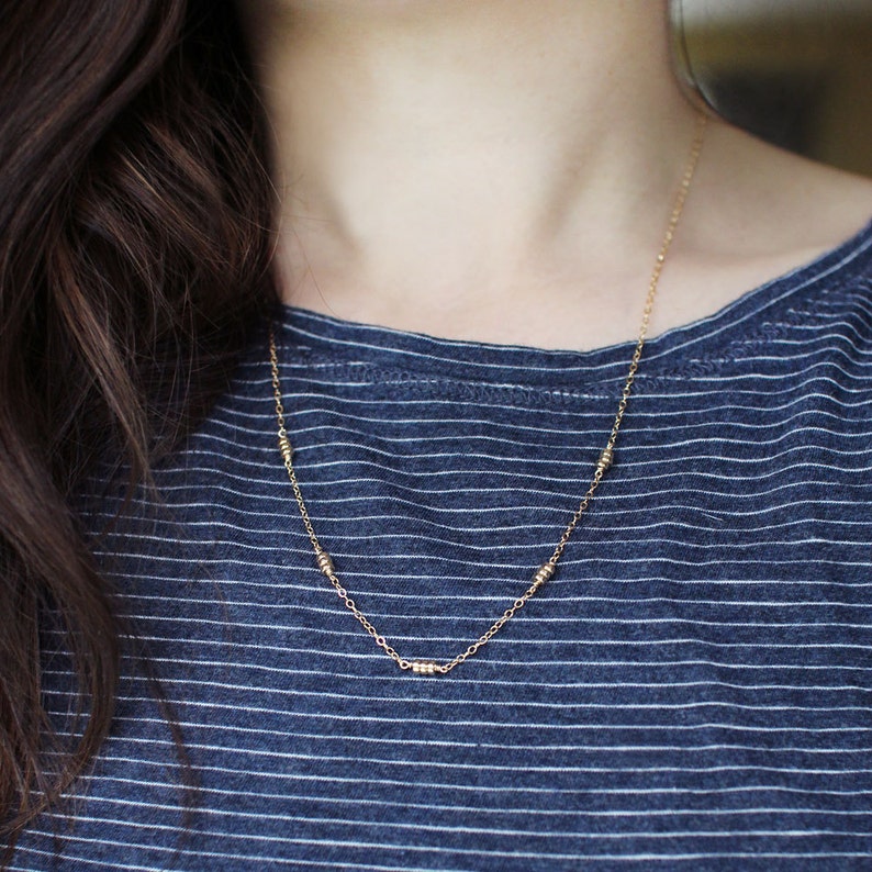 May include: A gold chain necklace with small, round beads. The necklace is worn by a person with long, dark hair.