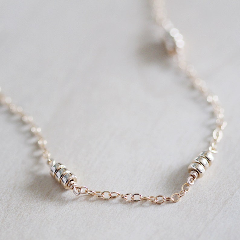 May include: A delicate gold chain necklace with three silver beads. The chain is made of small, linked circles.