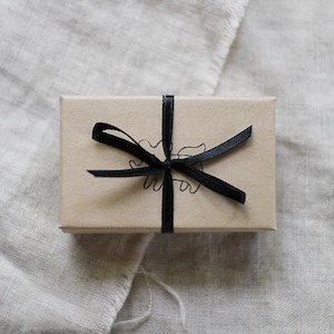 May include: A small brown box with a black ribbon tied in a bow. The box has a simple black line drawing of a creature on the front.