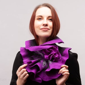 May include: A purple felted wool scarf with a large flower design. The scarf is worn around the neck of a person with red hair.