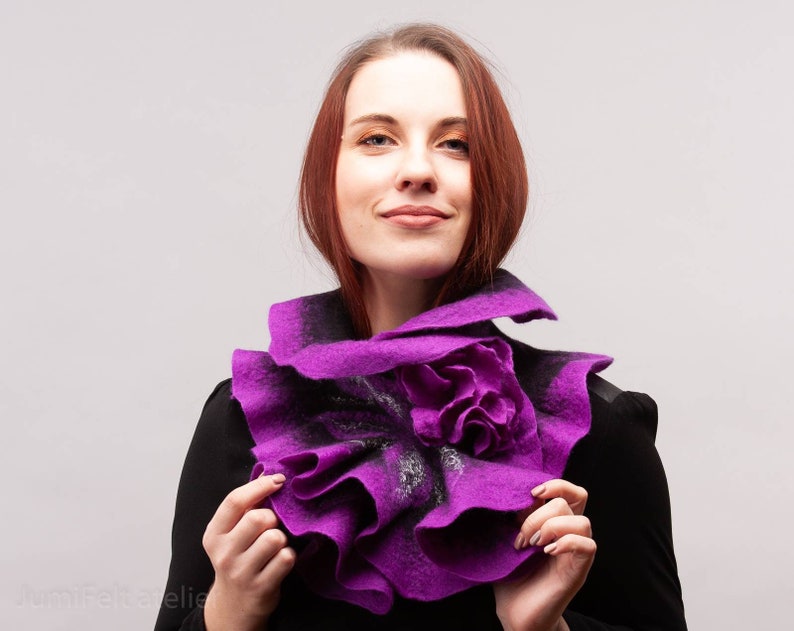 May include: A purple felted wool scarf with a large flower design. The scarf is worn around the neck of a person with red hair.