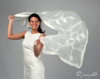 May include: A woman in a white dress with a white sheer scarf with a leaf pattern blowing in the wind.