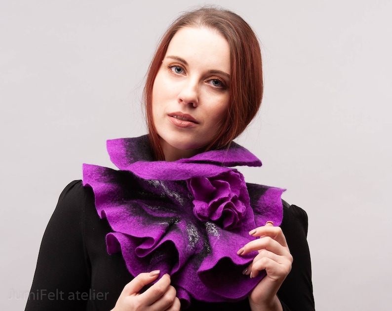 May include: A purple felted wool scarf with a ruffled design. The scarf has a large flower-shaped detail in the center.