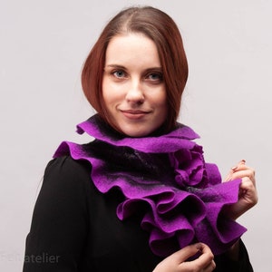 May include: A purple felted wool scarf with ruffled edges. The scarf is worn around the neck of a person.