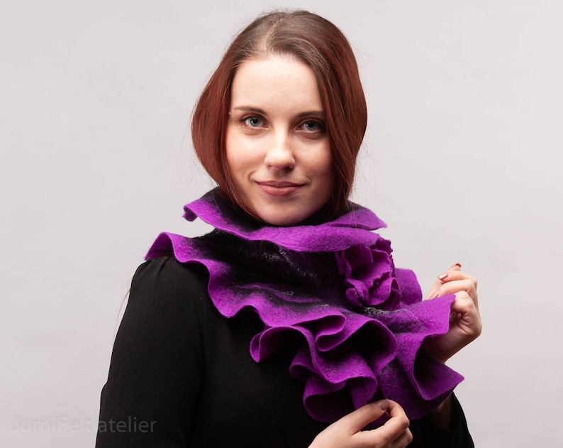 May include: A purple felted wool scarf with ruffled edges. The scarf is worn around the neck of a person.