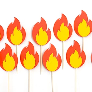 May include: A collection of twelve paper flame cutouts attached to thin wooden sticks. Each flame features a bright yellow center layered over a larger orange flame shape. The cutouts are arranged in two rows against a plain white background.