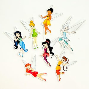 May include: A collection of seven die-cut stickers featuring cartoon fairies with wings, each depicted in a different color scheme including yellow, green, blue, red, purple, and white, arranged in a scattered pattern on a plain white background.