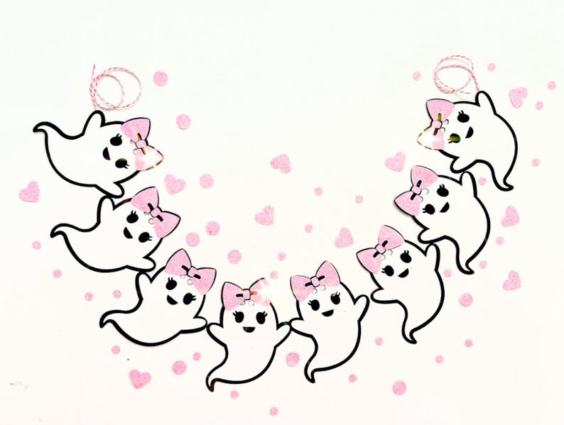May include: A garland of eight white ghosts with pink bows, each ghost has a black face with a smile and two black eyes. The ghosts are strung together with white twine and are on a white background with pink confetti.