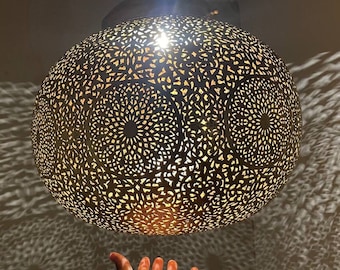 May include: A round, gold-coloured metal pendant light fixture with intricate cut-out designs. The light casts a pattern of light and shadow on the wall below.
