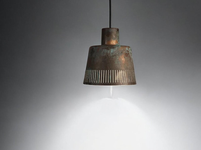 May include: A copper pendant light with a distressed finish and a perforated design. The light is casting a warm glow.