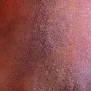 May include: Close-up of a textured, reddish-brown leather surface. The leather has a subtle sheen and a slightly grainy texture.