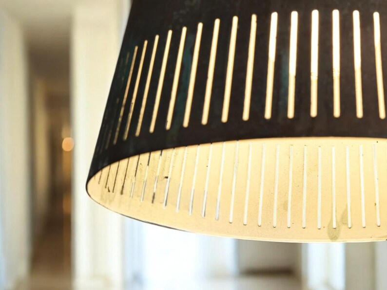 May include: A close-up of a black and white striped lampshade with a white interior. The lampshade is made of a thin, perforated material.