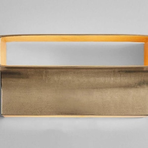 May include: A rectangular brass wall sconce with a slightly curved bottom edge. The sconce has a warm, golden finish and a subtle, textured surface.