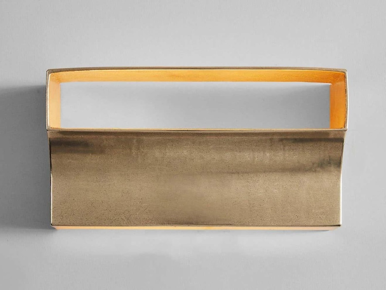 May include: A rectangular brass wall sconce with a slightly curved bottom edge. The sconce has a warm, golden finish and a subtle, textured surface.