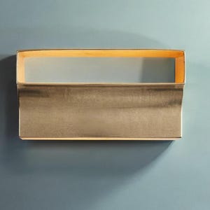 May include: A gold-toned wall sconce with a rectangular shape and a curved bottom edge. The sconce has a light inside that illuminates the room.