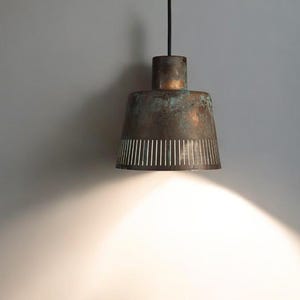 May include: A copper pendant light with a white patterned shade hangs from a black cord against a white wall.