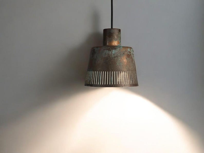 May include: A copper pendant light with a white patterned shade hangs from a black cord against a white wall.