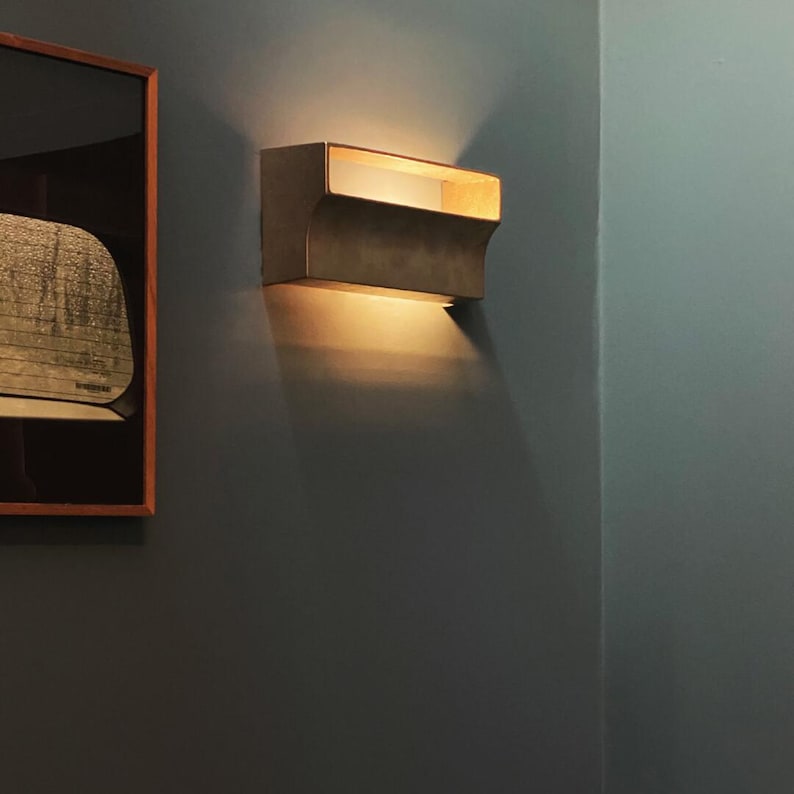 May include: A rectangular wall sconce with a warm, golden finish. The light fixture has a unique, curved design and emits a soft, warm glow.