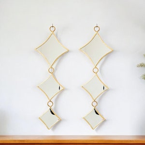 Könnte beinhalten: Zwei goldgerahmte Spiegel mit rautenförmigen Glasscheiben hängen an einer weißen Wand. Die Spiegel sind durch Ringe miteinander verbunden und erzeugen so einen kaskadierenden Effekt.