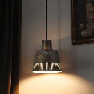 May include: A copper pendant light with a perforated shade hangs from a black cord. The light is on and casting a warm glow.