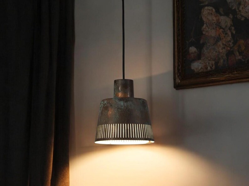 May include: A copper pendant light with a perforated shade hangs from a black cord. The light is on and casting a warm glow.