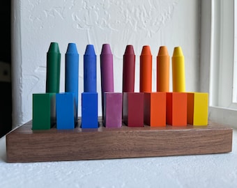 Könnte beinhalten: Ein Holzhalter mit 10 bunten Stiften, die in einem Regenbogenmuster angeordnet sind. Die Stifte befinden sich in einem Holzhalter mit Fächern für jeden Stift.