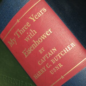May include: A red book cover with gold lettering that reads "My Three Years with Eisenhower" by Captain Harry C. Butcher USNR.