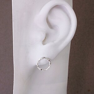 May include: A pair of silver hoop earrings with a textured finish. The earrings are small and delicate, and they are shown on a white mannequin head.