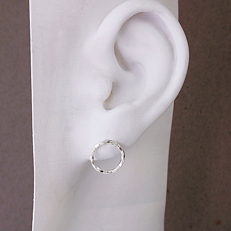 May include: A pair of silver hoop earrings with a textured finish. The earrings are small and delicate, and they are shown on a white mannequin head.