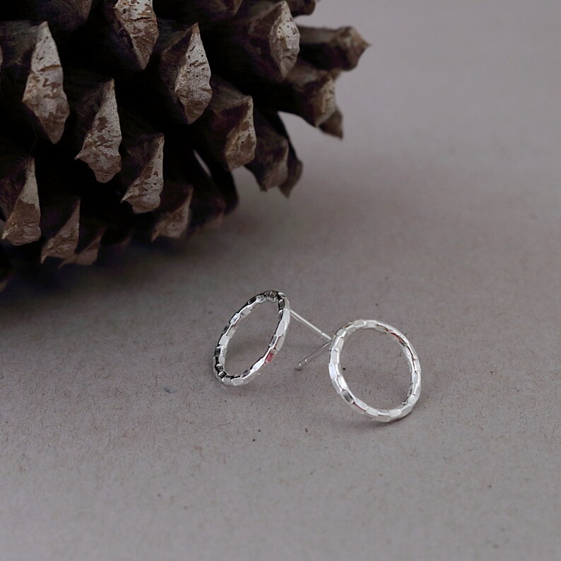 May include: A pair of silver stud earrings with a textured circular design.