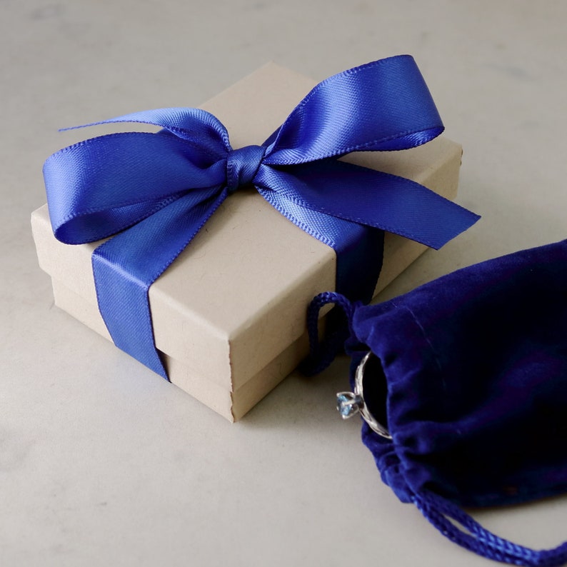 May include: A small, brown gift box tied with a blue satin ribbon. The box is sitting on a white surface next to a small, blue velvet pouch.