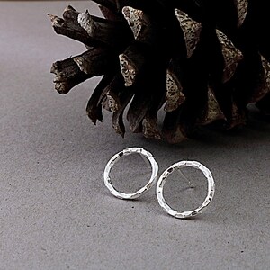 May include: A pair of silver textured hoop earrings. The earrings are small and delicate, and they have a hammered finish.