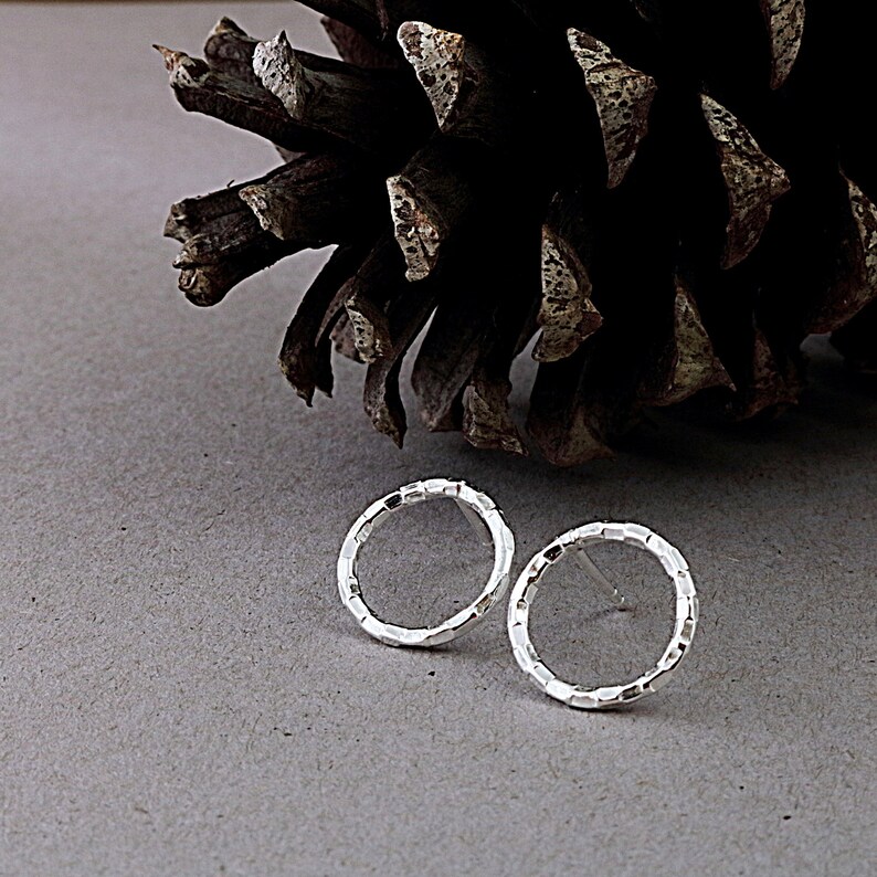 May include: A pair of silver textured hoop earrings. The earrings are small and delicate, and they have a hammered finish.