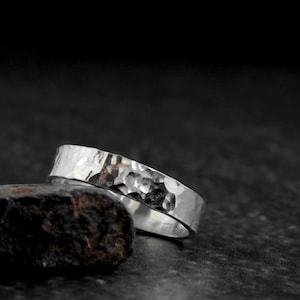 May include: A silver hammered band ring with a textured surface.