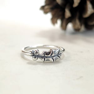 May include: A silver ring with a holly leaf and berry design.